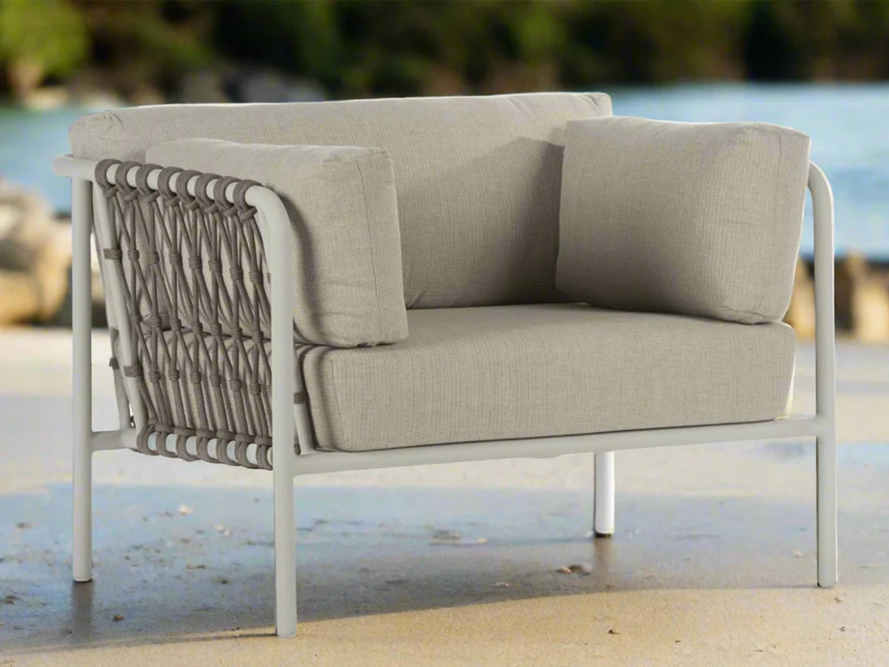 Beige outdoor armchair with marine grade rope backrest on a sandy beach.
