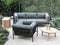 Outdoor patio set with gray sectional sofa, black chairs, and wooden coffee table in a garden setting.