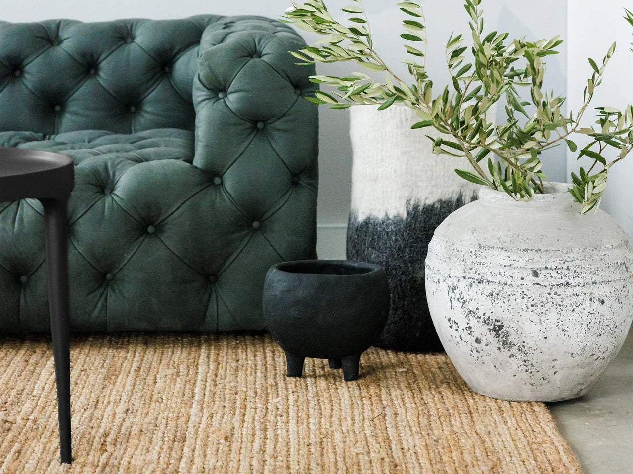 Green sofa next to 3 pot plants sitting on a large jute rug