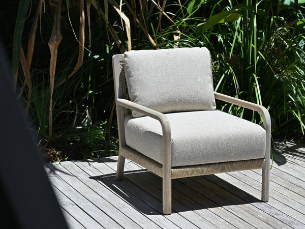Chair with light gray cushions on a wooden deck surrounded by greenery