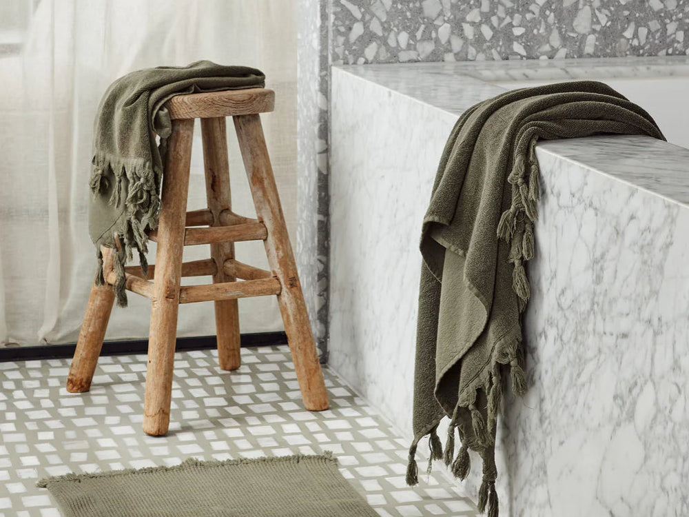 Bathroom with a wooden stool, saarde olive vintage collection bath sheet, hand towel and bath mat.