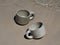 Two ceramic cups on a sandy beach with water in the background