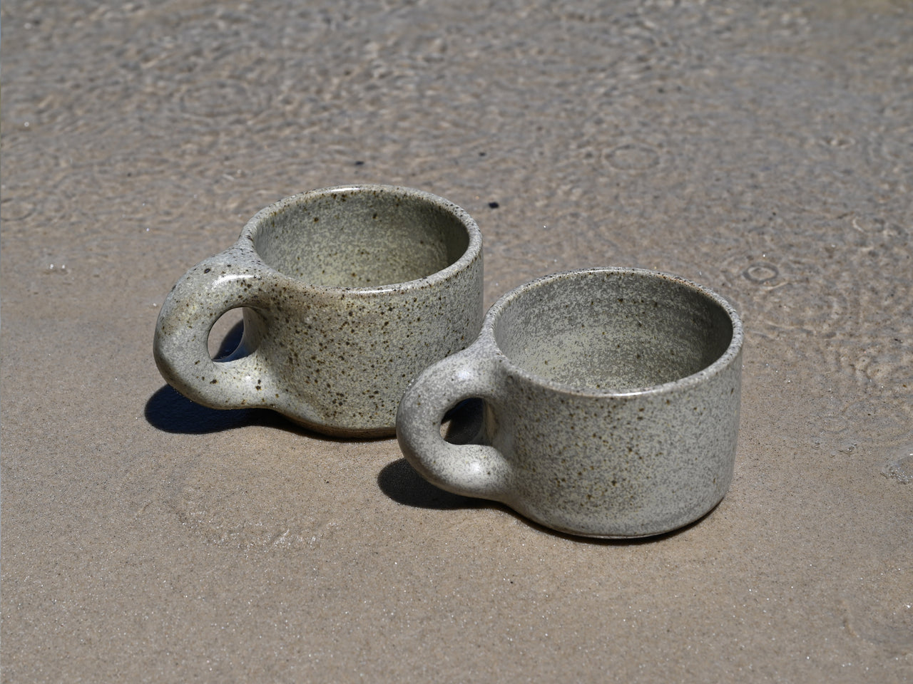 Two ceramic mugs on a sandy surface
