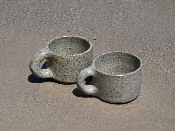Two ceramic mugs on a sandy surface
