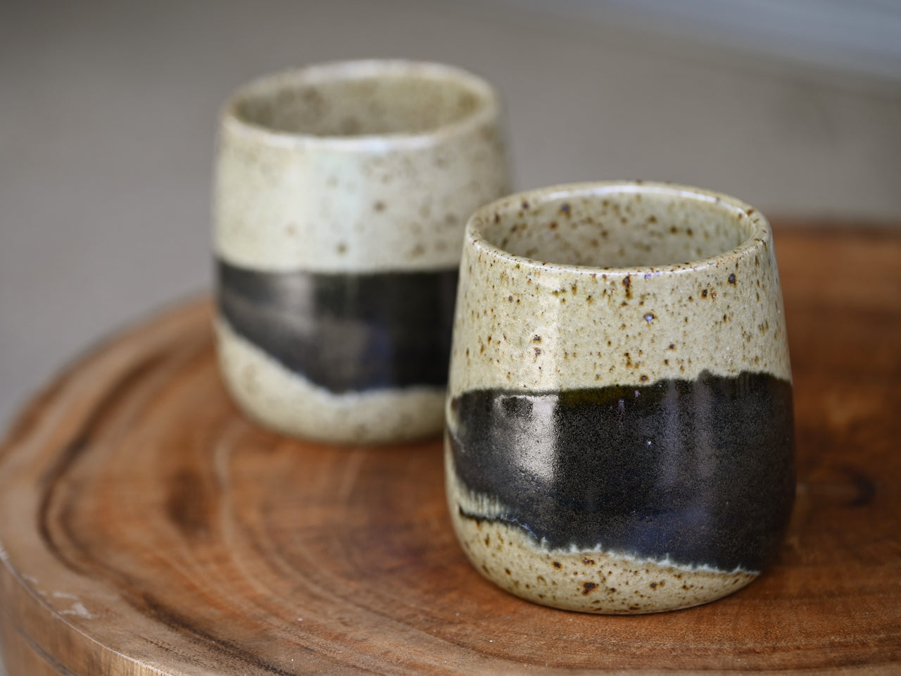 Two ceramic cups with black bands on a wooden surface