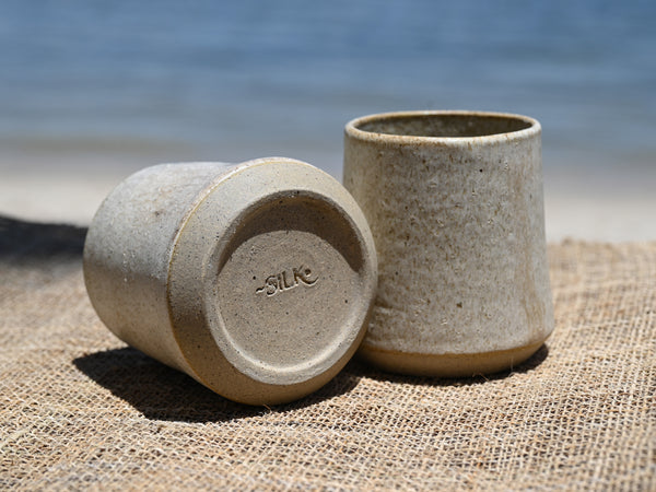 Two ceramic cups on a textured surface with a blurred natural background