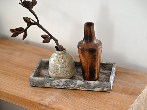 Decorative arrangement with a wooden vase, ceramic pot, and branch on a marble tray.