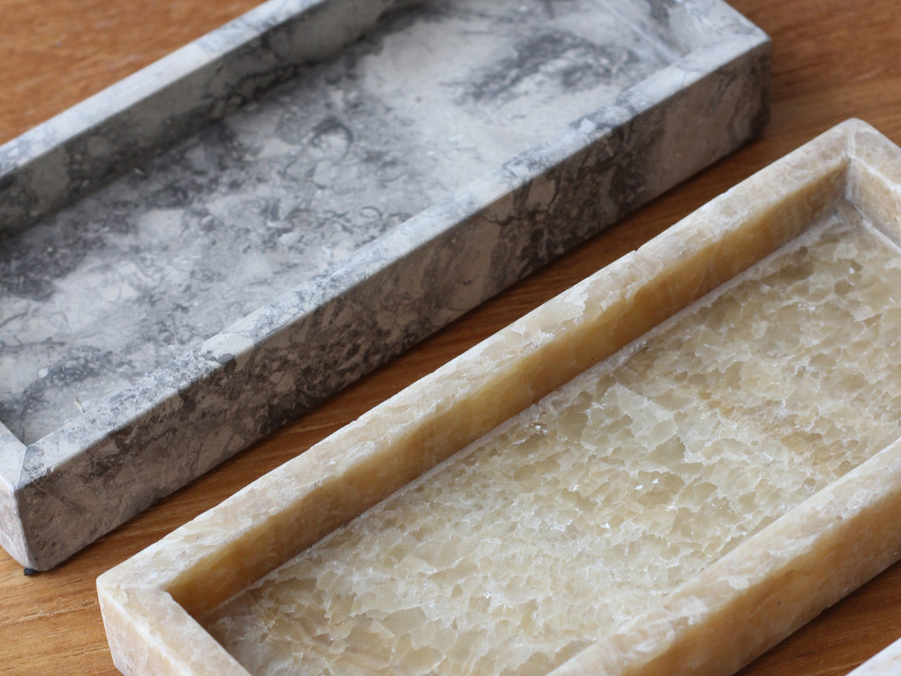 Two stone trays, one marble and one onyx, on a wooden surface.