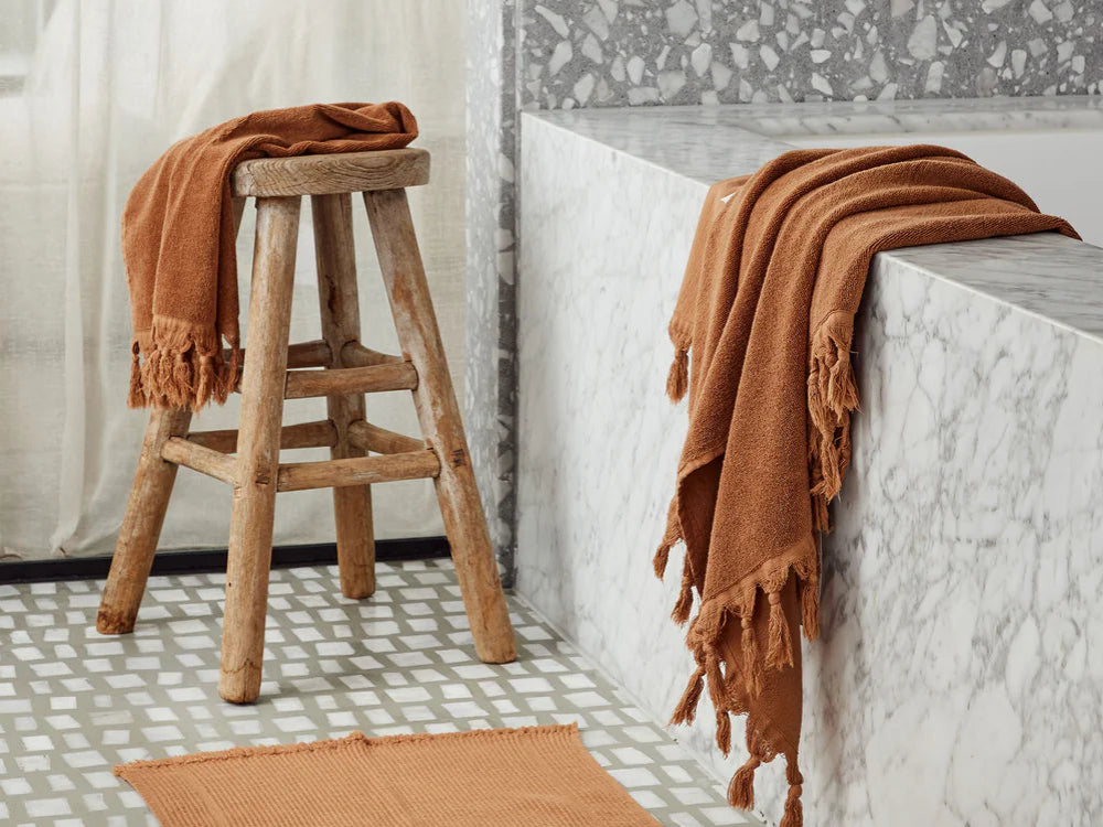 Bathroom with terrazzo tiles, a bathtub, and a stool with a towel, hand towel and bathmat.