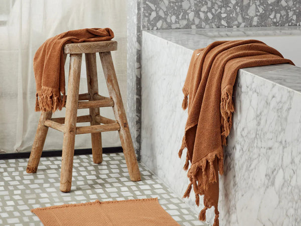 Bathroom with terrazzo tiles, a bathtub, and a stool with a towel, hand towel and bathmat.