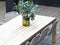 Outdoor dining table with chairs and a vase of greenery on a wooden deck.